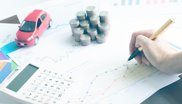 papeles con gráficos para ver el baremo de accidentes 2023 con calculadora, monedas y un coche al lado